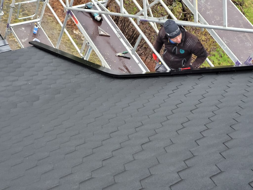 Fagperson i arbeid med tekking av mønet på det bratte taket